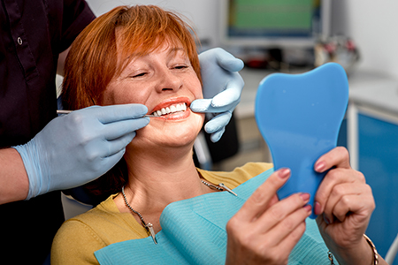 A woman wearing a blue mask with a smiley face on it, taking a selfie while sitting in a dental chair during a dental appointment.